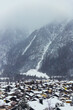 View of a snow-covered village nestled beneath towering, snow-dusted mountains under a grey sky, the rooftops capped with white, in Mittenwald, Bavaria, Germany.