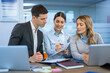 © Bojan - Female colleague explaining report to her business team while they listen attentively during a meeting in a beautiful blue office