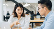 © Karmiyem - Two young Asian business professionals discussing project strategy in modern office environment teamwork collaboration