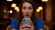© rdkcho - Woman with wide eyes and open mouth holding a smartphone Overhead lights create bokeh