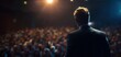 © Studio Nova - The Speaker Standing on Stage Facing a Large Blurred Audience Under Spotlights