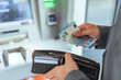 © Dragana Gordic - Individual Withdraws Cash at an ATM While Holding Wallet and Euro Notes
