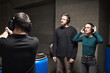 © DragonImages - Caucasian young adult man and Caucasian young adult woman standing at indoor shooting range wearing protective headphones and glasses while instructor demonstrating firearm handling