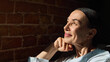 © Lustre Art Group  - Mature woman in white shirt smiling towards sunlight near brick wall. Concept of skincare, aging wellness, lifestyle positivity and natural grace with hopeful emotion.