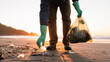 © artforwarm - A person wearing green gloves is picking up plastic waste on a polluted beach during sunset.