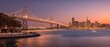 A stunning view of San Francisco’s Bay Bridge and skyline at sunset, with calm waters reflecting city lights