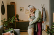 © AnnaStills - Senior Caucasian woman embracing smiling Caucasian child in cozy living room, both standing and showing affection, plants and wall decor visible in background