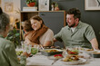© AnnaStills - Caucasian young woman hugging child while sitting at dining table with middle aged Caucasian man and senior woman, sharing family meal and enjoying togetherness during gathering
