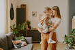 © AnnaStills - Caucasian young adult woman holding Caucasian child boy with stuffed animal, standing close together and smiling in modern living room, plants and decor visible in background