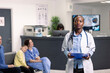 © DC Studio - Portrait of african american doctor holding clipboard and standing in hospital lobby. Confident black female physician looking at camera, ready to provide medical consultation to patients.