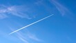 © Ikam - A wispy, white contrail stretches across a vibrant, cerulean sky, dotted with delicate clouds.