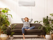 © New Africa - Woman relaxing on sofa surrounded by potted houseplants at home. Air conditioner keeping comfortable temperature in room