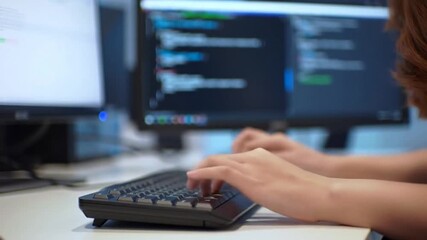 Person diligently coding, hands actively typing on keyboard, focused on dual computer screens displaying lines of code.