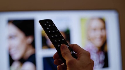 Close-up shot of a hand holding a remote, pointed at a TV screen displaying various video streaming apps. Low-angle perspective.