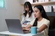 © itchaznong - Focused Learning. Young woman working on a laptop while her sister observes.