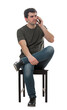 © 1STunningART - Dissatisfied young man sitting on chair talking on phone. Thoughtful male seated full length portrait isolated on transparent background