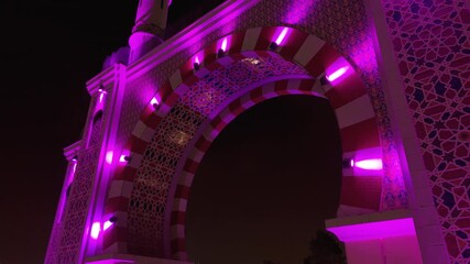 Wall Mural - An aerial close-up shot reveals the intricate Moorish patterns and architectural details of the Arco de la Amistad, illuminated by vibrant purple lights at night in Lima, Peru