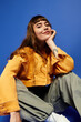 © Bliss - Stylish young woman in vibrant attire poses against a striking blue backdrop with confidence