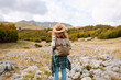 © maxbelchenko - A rear view of a female hiker with a backpack and a hat walking along a rocky trail at sunset. Young woman enjoying the mountain scenery, admiring the views. Adventure, freedom and weekend concept.