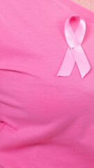 Wall Mural - Video of midsection of caucasian woman wearing pink cancer awareness ribbon, with pink background