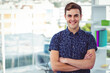 © wavebreak3 - Man standing with arms crossed at office desk by window showing urban skyline, shelving unit