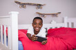 © wavebreak3 - Smiling boy playing with smartphone on bed, surrounded by skateboards at home, copy space