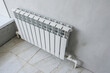 © evgeniykleymenov - A white radiator is installed against a gray wall, on a tiled floor. The room appears to be under renovation