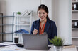 © David - Portrait of an Asian young Female working on a laptop computer in workplace office, Asian woman happy hold notebook and pen at desk.