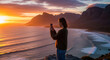 © W.O.W - Woman capturing a scenic sunset view over the ocean with a smartphone. Travel adventure and relaxation, a moment to remember nature's beauty.