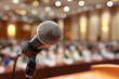 © Ima - Microphone poised on stage for speaker at conference before large audience