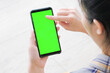 © Frd69 - Over the shoulder view of a woman's hands holding a smartphone with a blank green screen, touching the display for a mobile app mockup