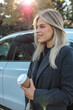 © shine.graphics - Blonde woman enjoying a coffee break next to a car on a sunny day.