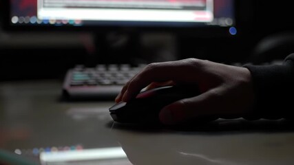 Computer Work: Man uses mouse to navigate illuminated computer screen in a darkened home office environment.