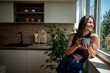 © Migma_Agency - Young woman enjoying a cup of coffee by the window in a modern kitchen