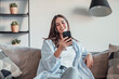 © Daniel - Smiling woman looking at smartphone screen, sitting on couch, enjoying leisure time with mobile device at home, happy young female chatting in social network or surfing internet, shopping online