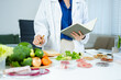 © Nuttapong punna - Female nutritionist in lab coat analyzing food and writing in notebook. Healthy eating, organic testing, and nutrition science in a clean lab.