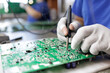© st.kolesnikov - Gloved technician hand soldering components on printed circuit board in factory