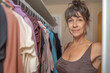 © sam richter - Middle-aged woman standing beside organized clothing rack in walk-in closet space.