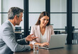 © InfinityVisuals - Business discussion at the office: Two professionals, a man and woman, are engaged in a focused business discussion around a laptop at a modern office.