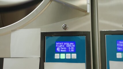 Close zoom on control panel buttons of industrial laundry washer, showcasing display and settings as camera pushes toward interface; stainless rim and glass door visible, clean laundromat equipment