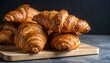 © Ataur - Golden Brown Croissants Stacked on Rustic Wooden Board, Generated image