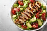 Grilled chicken salad with avocado and tomatoes in a white bowl on a light background, top view, flat lay. Healthy food idea. Concept for healthy eating, weight loss, or body-building advertising