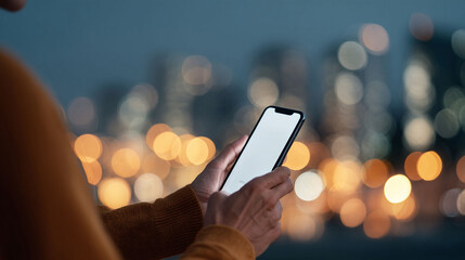 Person using a smartphone with blank screen at night. Urban backdrop bokeh lights. Good for technology, communication, and modern lifestyle concepts.
