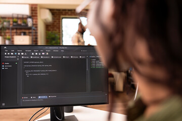 Closeup of black freelance developer using desktop pc to debug and refine website code. Rearview of remote tech entrepreneur managing programming tasks on computer from home.