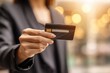 © whitestorm - Woman in a suit holds out a credit card for payment in a brightly lit environment, suggesting financial transactions and modern commerce.