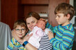 © Irina Schmidt - Mother holding newborn baby girl in hospital bed, with two sons sitting beside her. Real life, real people moment of family love, siblings bonding, and joy of welcoming a new child.