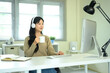 © Prathankarnpap - Young Asian woman wearing headphones, drinking coffee, and working on computer in home office