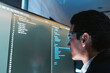 © artitwpd - Software developer wearing glasses focuses on code displayed on a large monitor in a modern office, reviewing and debugging source files on a wide screen workstation.