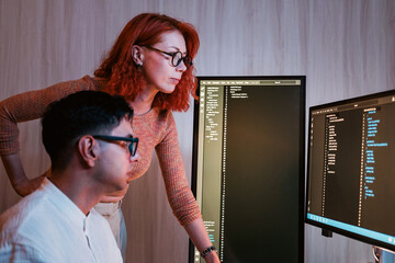 two colleagues analyze code on dual monitors in a modern office, collaborating on software developme