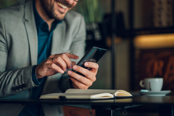 Businessman using smartphone and smiling in cafe